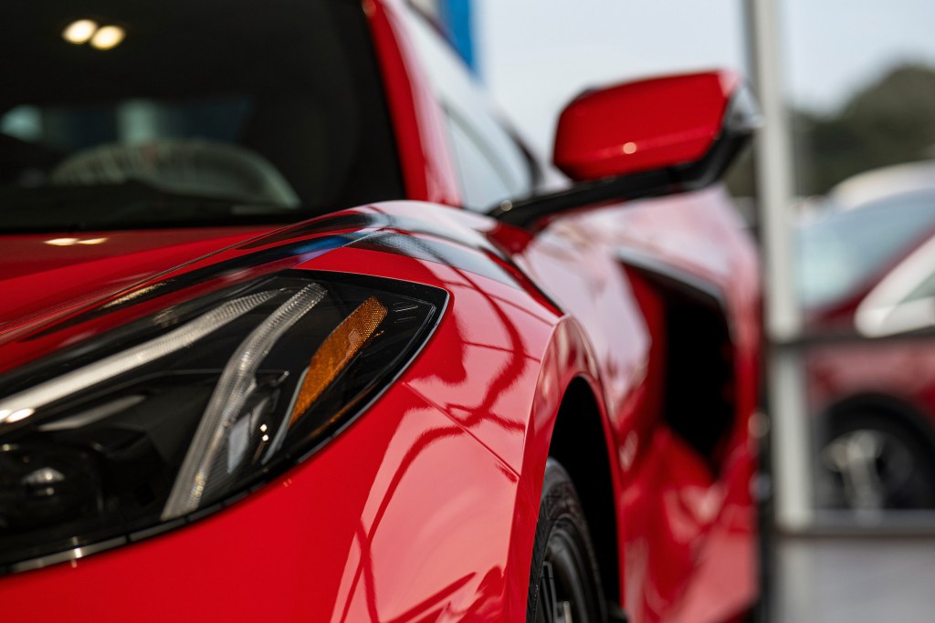 A close-up of a red 2021 Chevy Corvette's driver's-side headlight, side-view mirror, and black side air intake