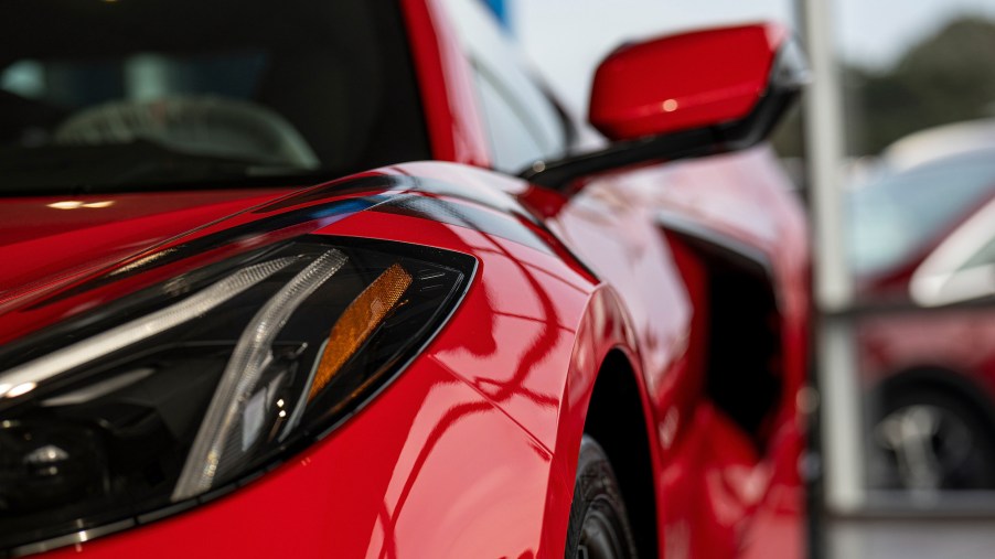 A close-up of a red 2021 Chevy Corvette's driver's-side headlight, side-view mirror, and black side air intake