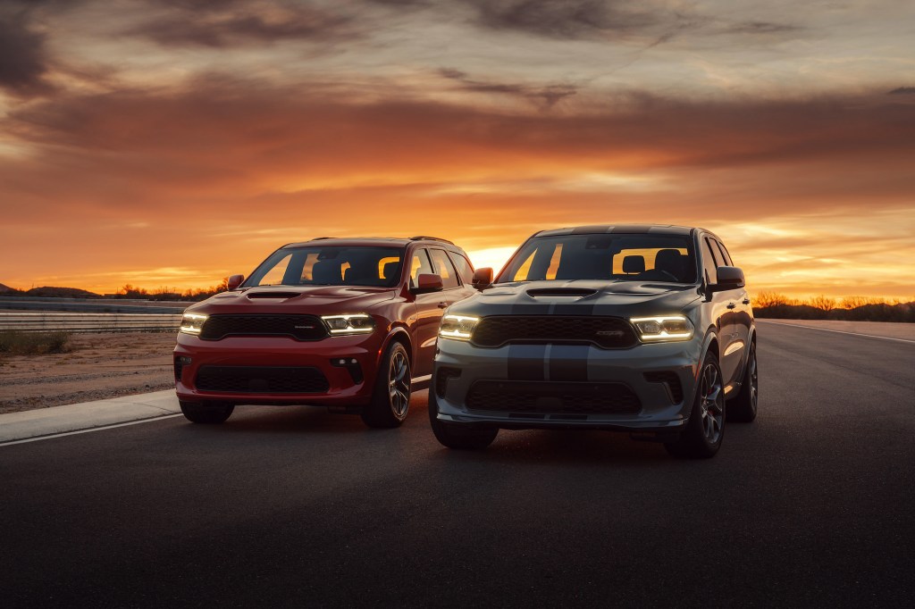 A red 2021 Dodge Durango R/T Tow N Go SUV (left) and a white-and-blue Durango SRT Hellcat SUV parked side-by-side on a racetrack at sunset