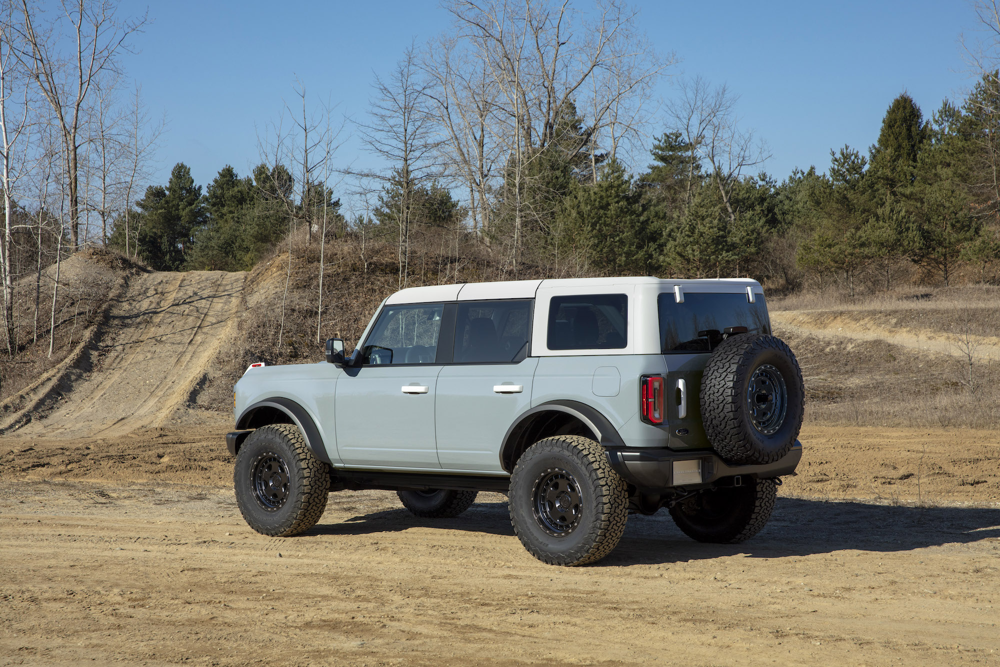 A four-door 2021 Ford Bronco SUV parked on a dirt trail near the woods