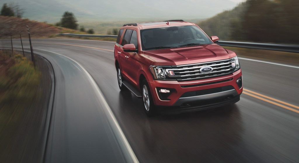 A red 2021 Ford Expedition full-size SUV travels on a two-lane highway up a mountain on a foggy day