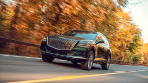 A dark-green 2021 Genesis GV80 travels on a tree-lined two-lane highway in Hudson Valley, New York