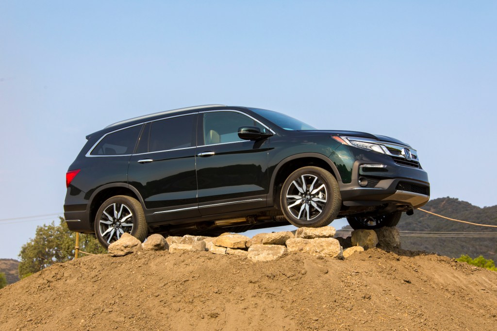 A dark-green metallic 2021 Honda Pilot Elite midsize crossover SUV parked on rocks atop a dirt mound