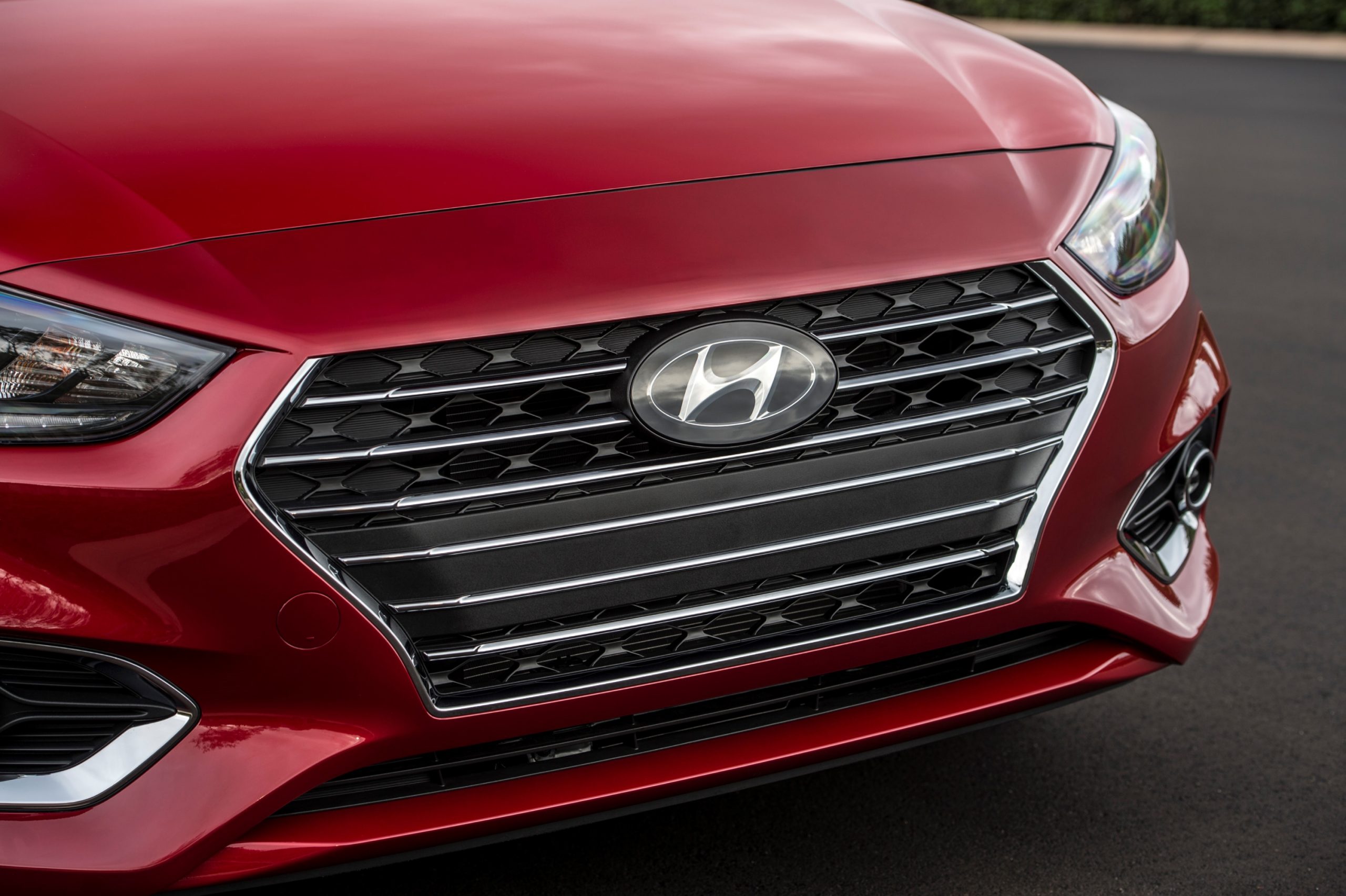 A close-up of the Hyundai logo on the grille of a red 2021 Accent subcompact car