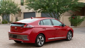 A red 2021 Hyundai Ioniq Hybrid four-door hatchback parked on beige brick pavers outside a tan-and-brown modern residence