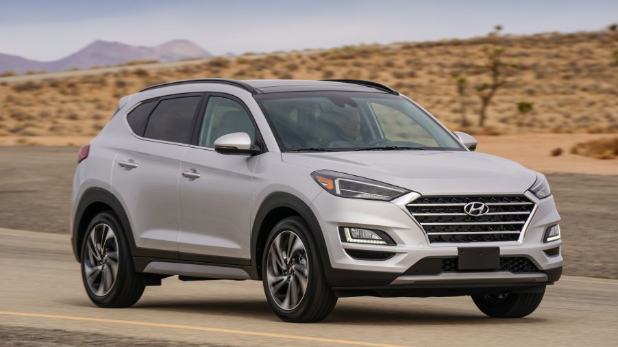 A silver 2021 Hyundai Tucson compact SUV travels on a desert road with mountains in the background