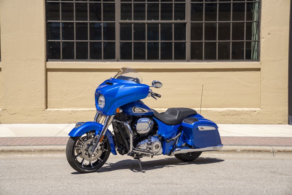 A blue 2021 Indian Chieftain Limited with accessory saddlebag speakers by a tan building