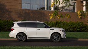 A white 2021 Infiniti QX80 three-row SUV parked along a curb next to grass and trees outside a modern office building