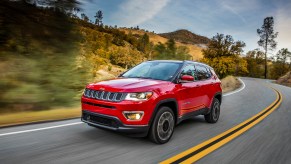 A red 2021 Jeep Compass Limited compact crossover SUV traveling on a two-lane highway through hills and trees
