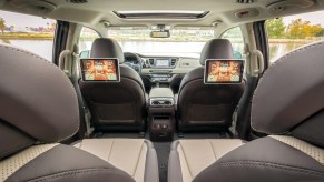 The brown and beige interior of a 2021 Kia Sedona minivan, shown from the third row looking forward
