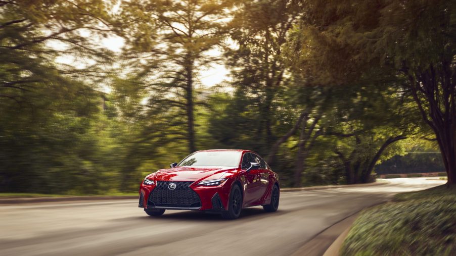 A red 2021 Lexus IS driving on a tree-lined road