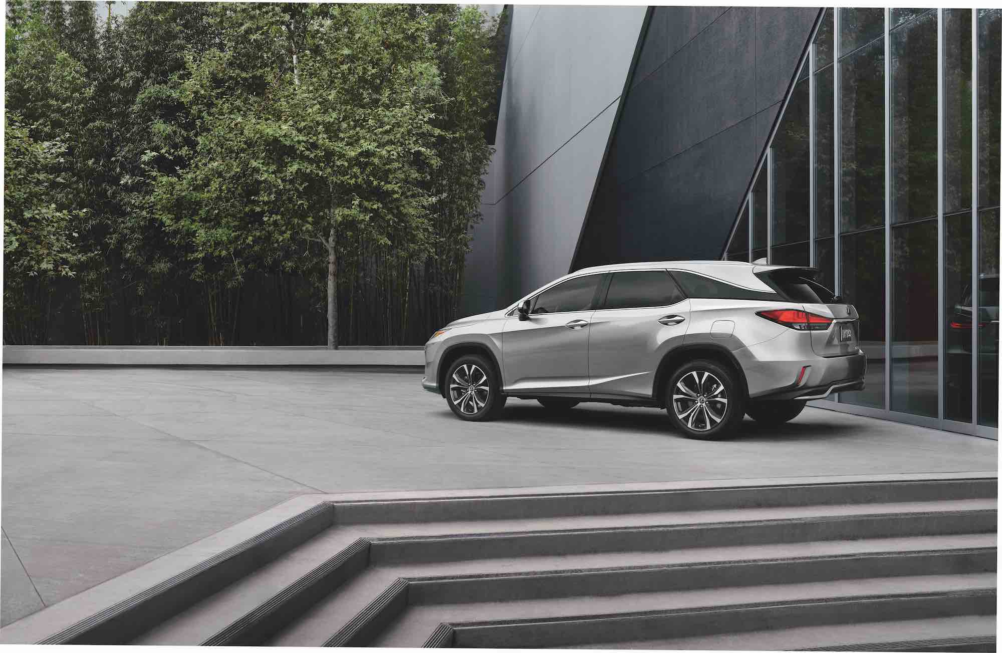 A silver 2021 Lexus RX L midsize luxury SUV parked at the top of some concrete steps next to a modern building and trees
