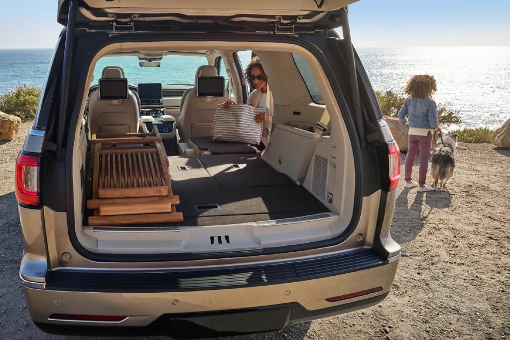 The rear view of the tan-leather interior of a 2021 Lincoln Navigator with its seats folded, loaded with folded wooden chairs by a beach