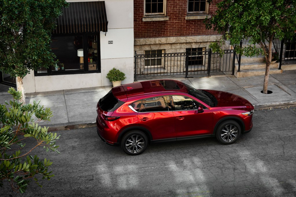 A red 2021 Mazda CX-5 parked on a tree-lined city street