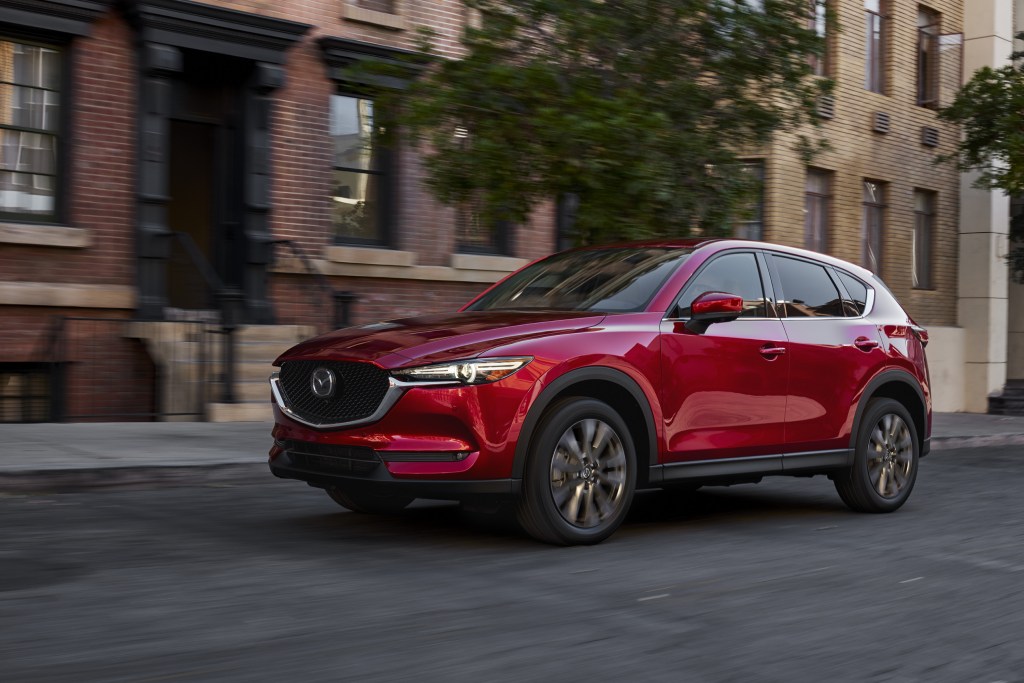 A red 2021 Mazda CX-5 driving down a city road with a building and tree in the background
