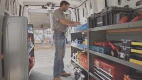 A man stands inside a white 2021 Nissan NV cargo van lined with shelves of tool chests and other work equipment