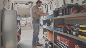A man stands inside a white 2021 Nissan NV cargo van lined with shelves of tool chests and other work equipment