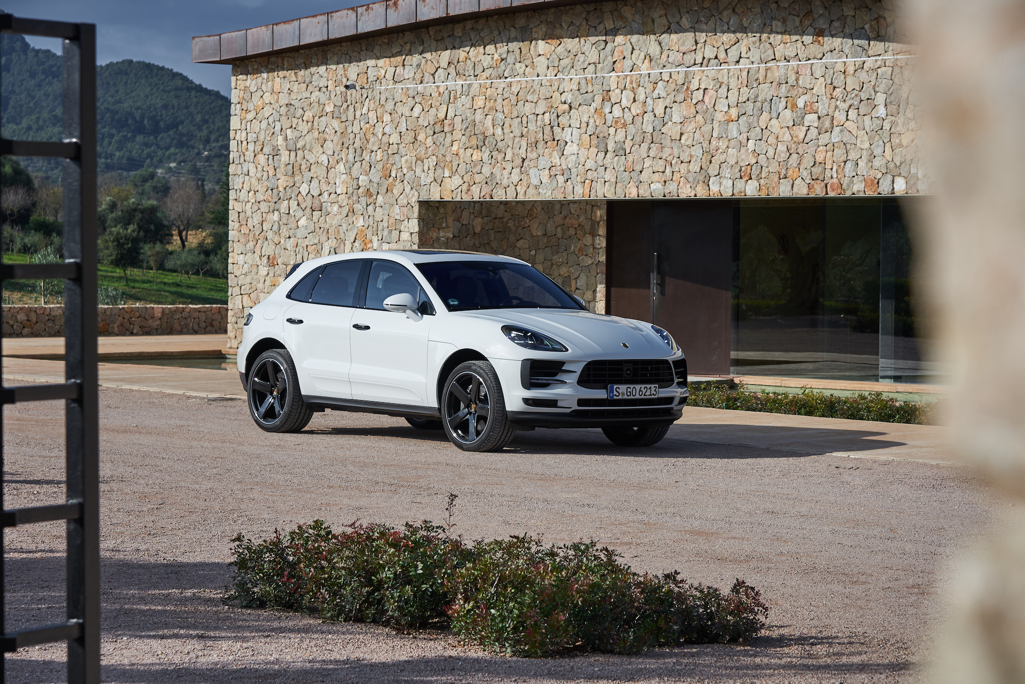 A white 2021 Porsche Macan luxury compact crossover SUV parked outside a stone building with mountains in the background