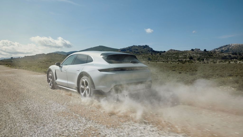 The rear 3/4 view of a white 2021 Porsche Taycan 4S Cross Turismo accelerating down a gravel road