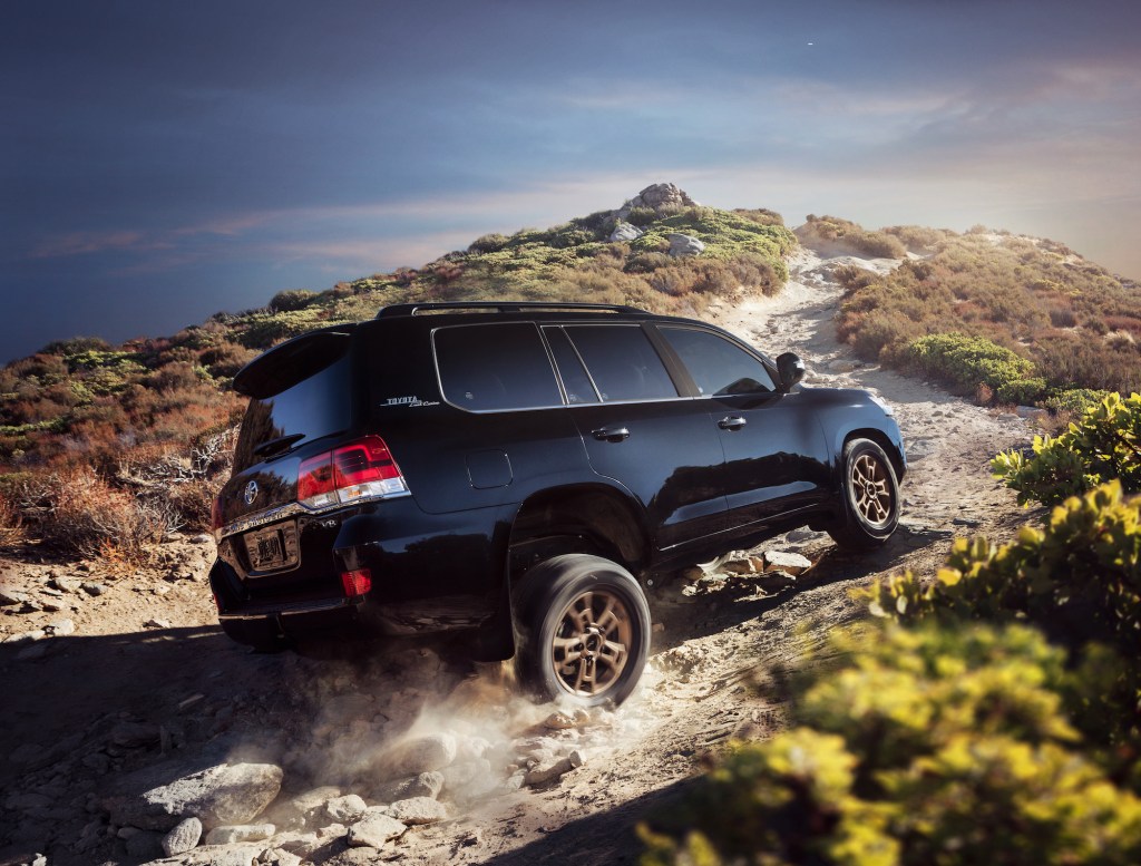 A black 2021 Toyota Land Cruiser four-wheel-drive full-size SUV travels on a dusty, rocky path up a hill
