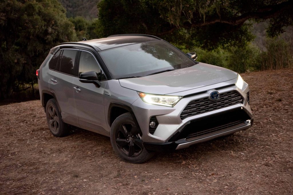 A silver 2021 Toyota RAV4 XSE Hybrid compact crossover SUV parked on the dirt in front of shrubs and trees