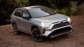 A silver 2021 Toyota RAV4 XSE Hybrid compact crossover SUV parked on the dirt in front of shrubs and trees