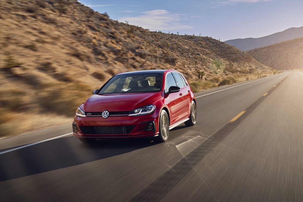 A red 2021 Volkswagen GTI four-door hatchback traveling on a two-lane highway through arid mountains on a sunny day