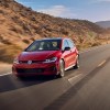 A red 2021 Volkswagen GTI four-door hatchback traveling on a two-lane highway through arid mountains on a sunny day