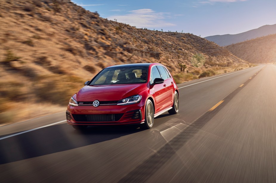 A red 2021 Volkswagen GTI four-door hatchback traveling on a two-lane highway through arid mountains on a sunny day