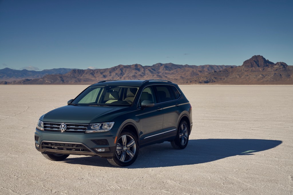 A dark-gray 2021 Volkswagen Tiguan compact crossover SUV parked in a desert with mountains in the background