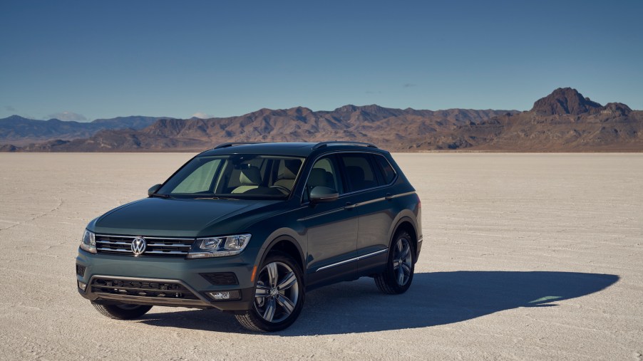 A dark-gray 2021 Volkswagen Tiguan compact crossover SUV parked in a desert with mountains in the background
