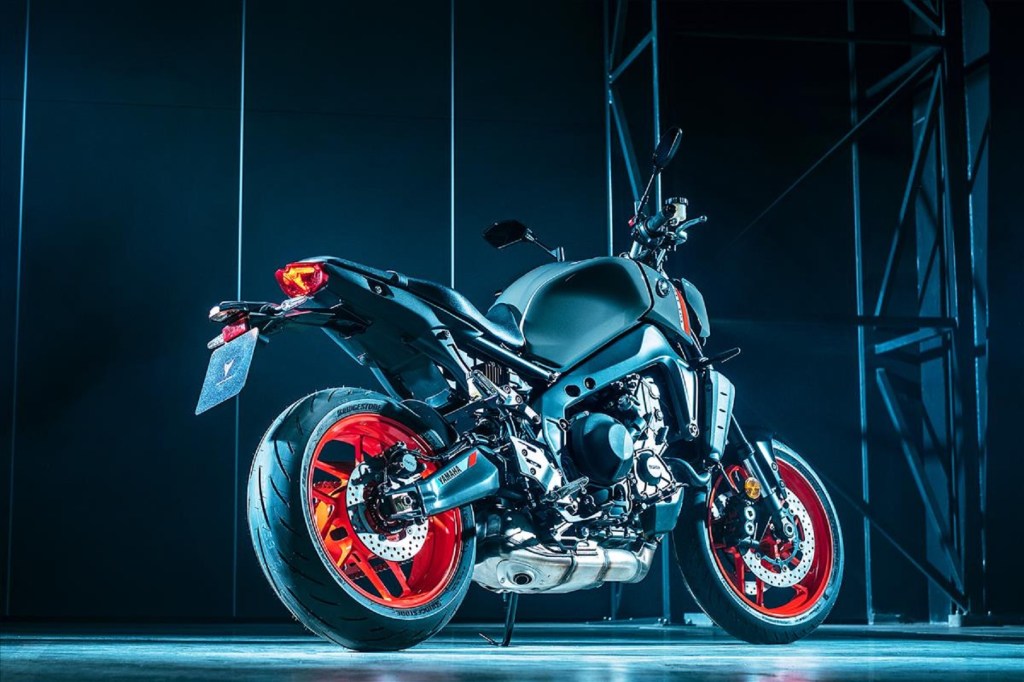 A low-angle rear 3/4 view of a gray-and-black-with-orange-wheels 2021 Yamaha MT-09 in a dark room