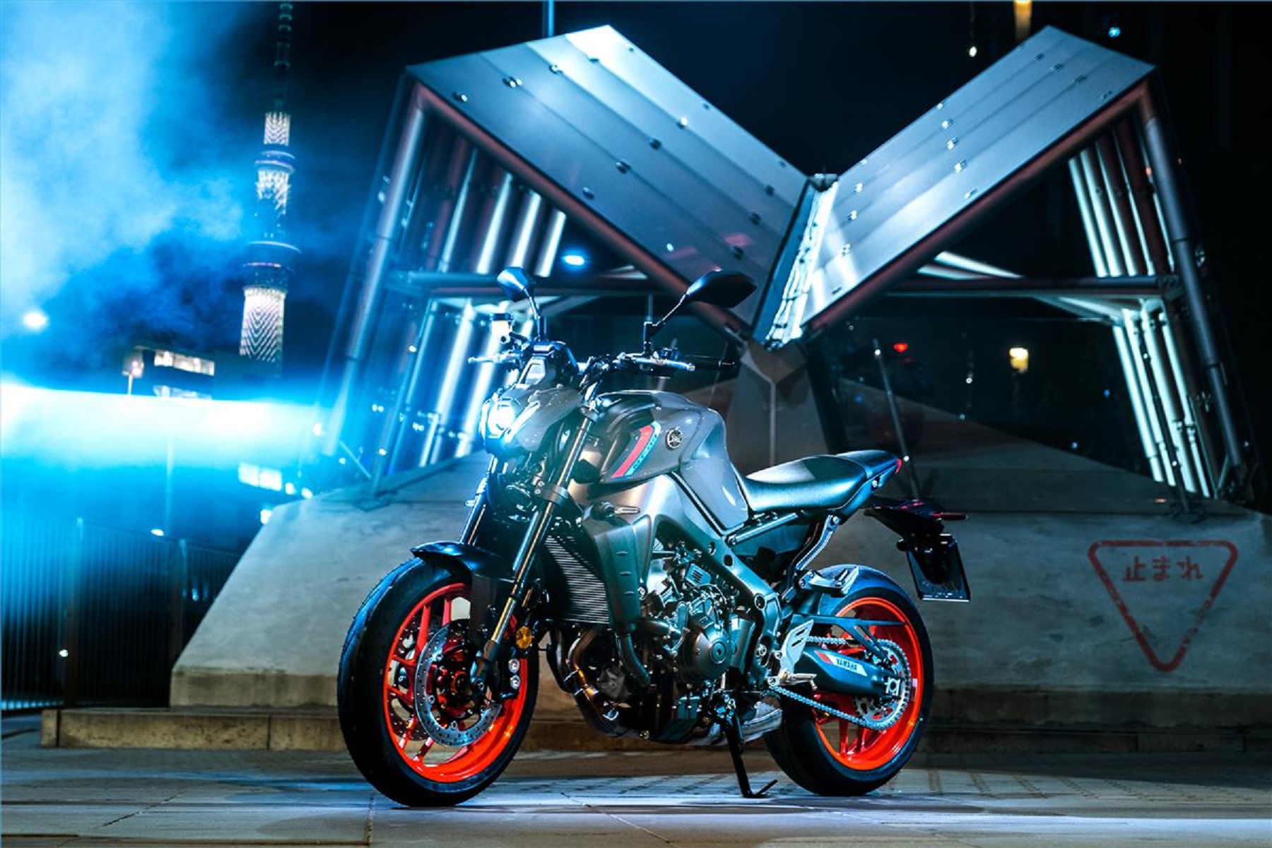 A gray-and-black-with-orange-wheels 2021 Yamaha MT-09 in front of a building at night