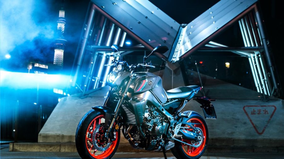 A gray-and-black-with-orange-wheels 2021 Yamaha MT-09 in front of a building at night
