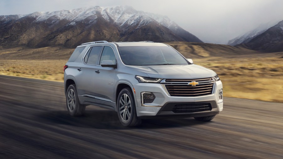 A light-colored 2022 Chevrolet Traverse High Country three-row midsize SUV traveling on a road past snow-capped mountains