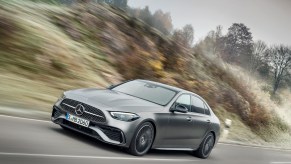 A 2022 Mercedes-Benz C-Class sedan with Selenite Grey Magno exterior paint travels on a highway along hills and trees