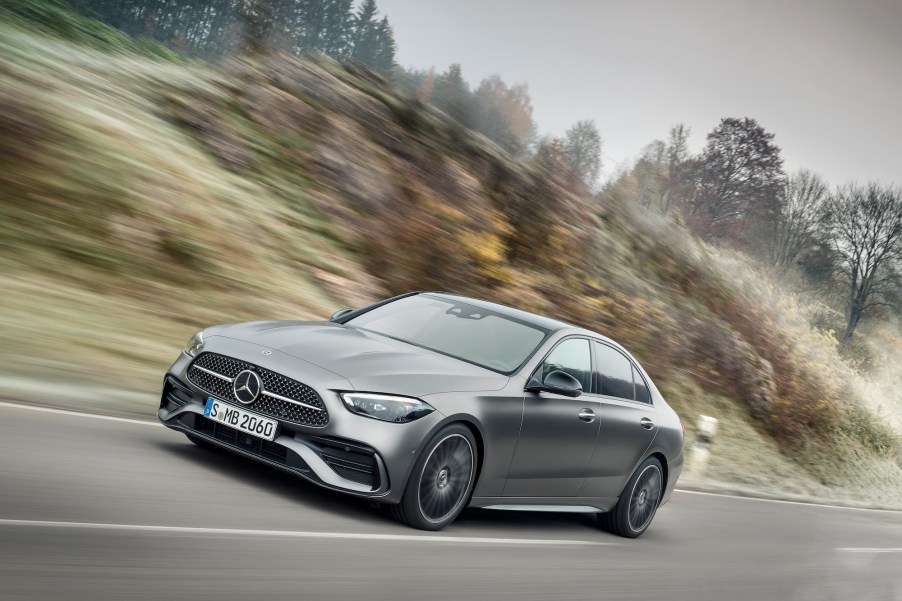 A 2022 Mercedes-Benz C-Class sedan with Selenite Grey Magno exterior paint travels on a highway along hills and trees