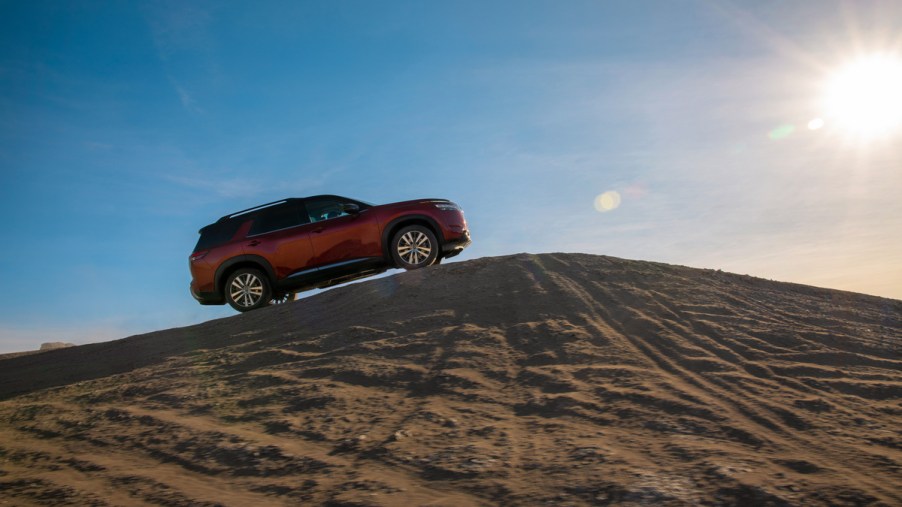 A red 2022 Nissan Pathfinder driving up a sand dune