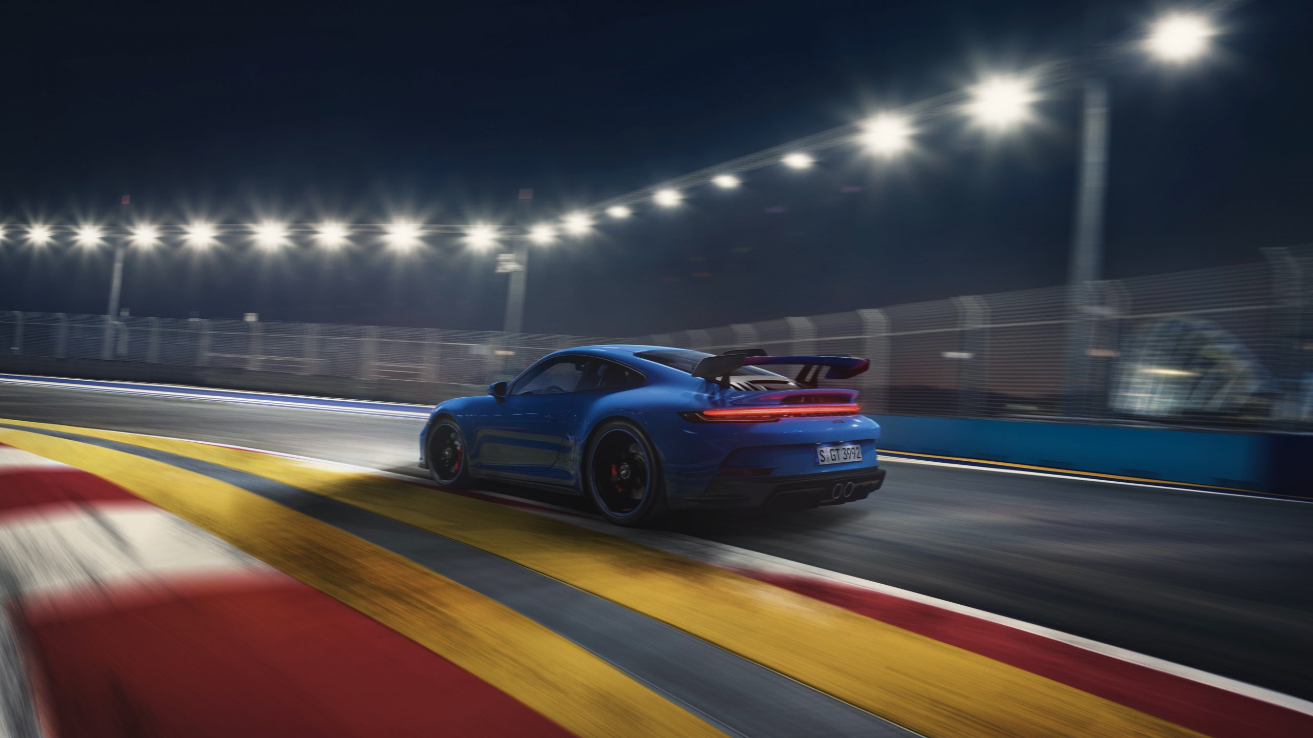 A blue 2022 Porsche 911 GT3 driving on a lit track at night