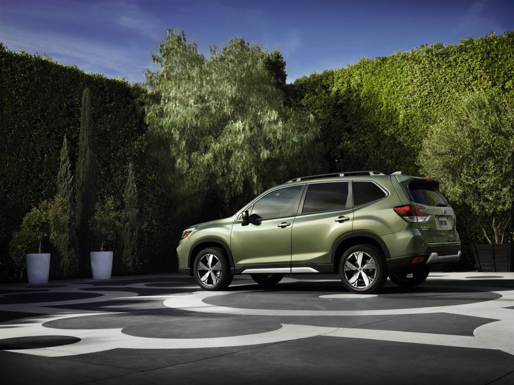 A green 2020-2021 Subaru Forester on display in a parking lot with green bushes in the background