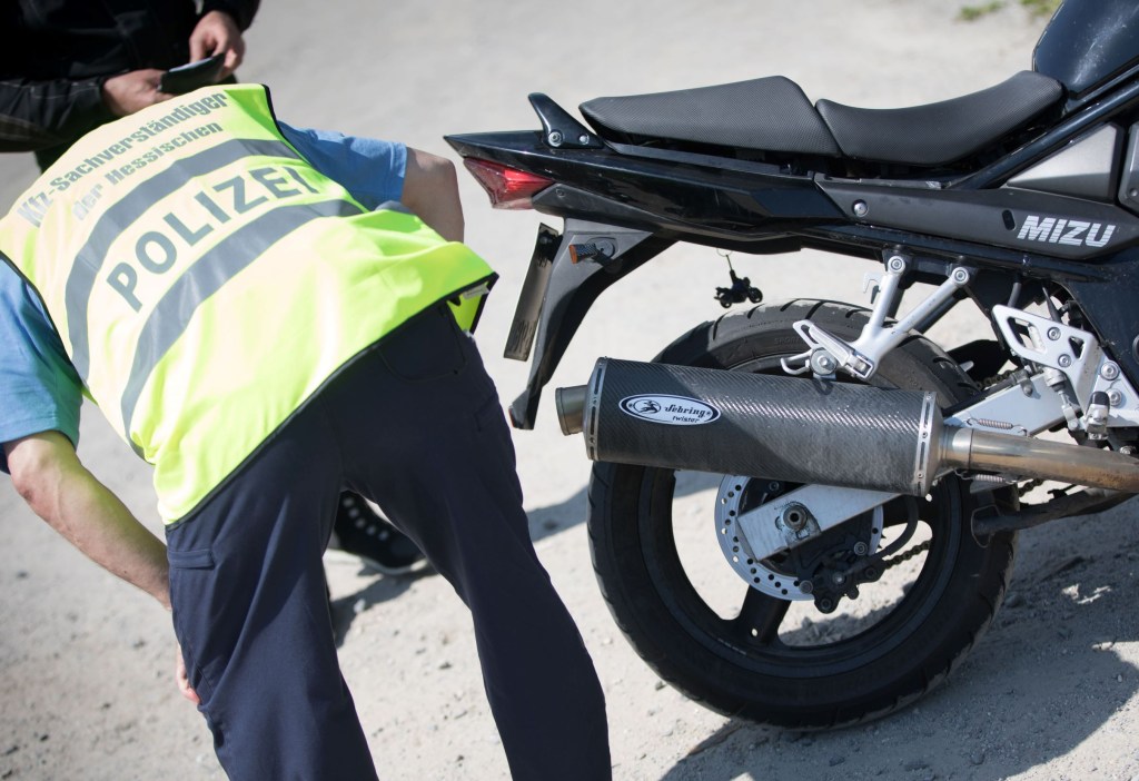 A German police officer in a high-vis jacket checks how loud a black motorcycle's exhaust pipe is