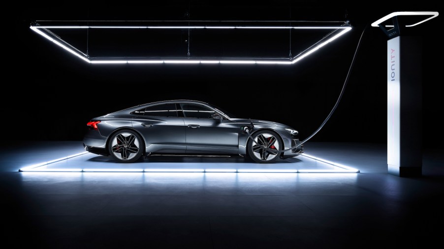 A dark metallic Audi e-tron GT electric four-door car parked under lights in a dark room
