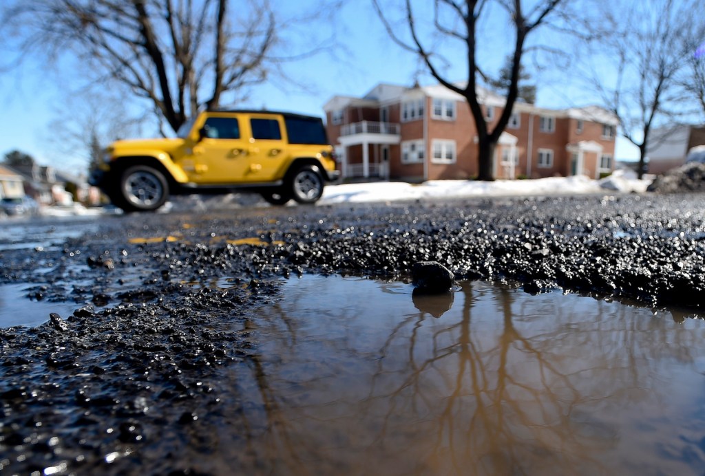 A Jeep Wrangler avoids hitting a pothole on a street.