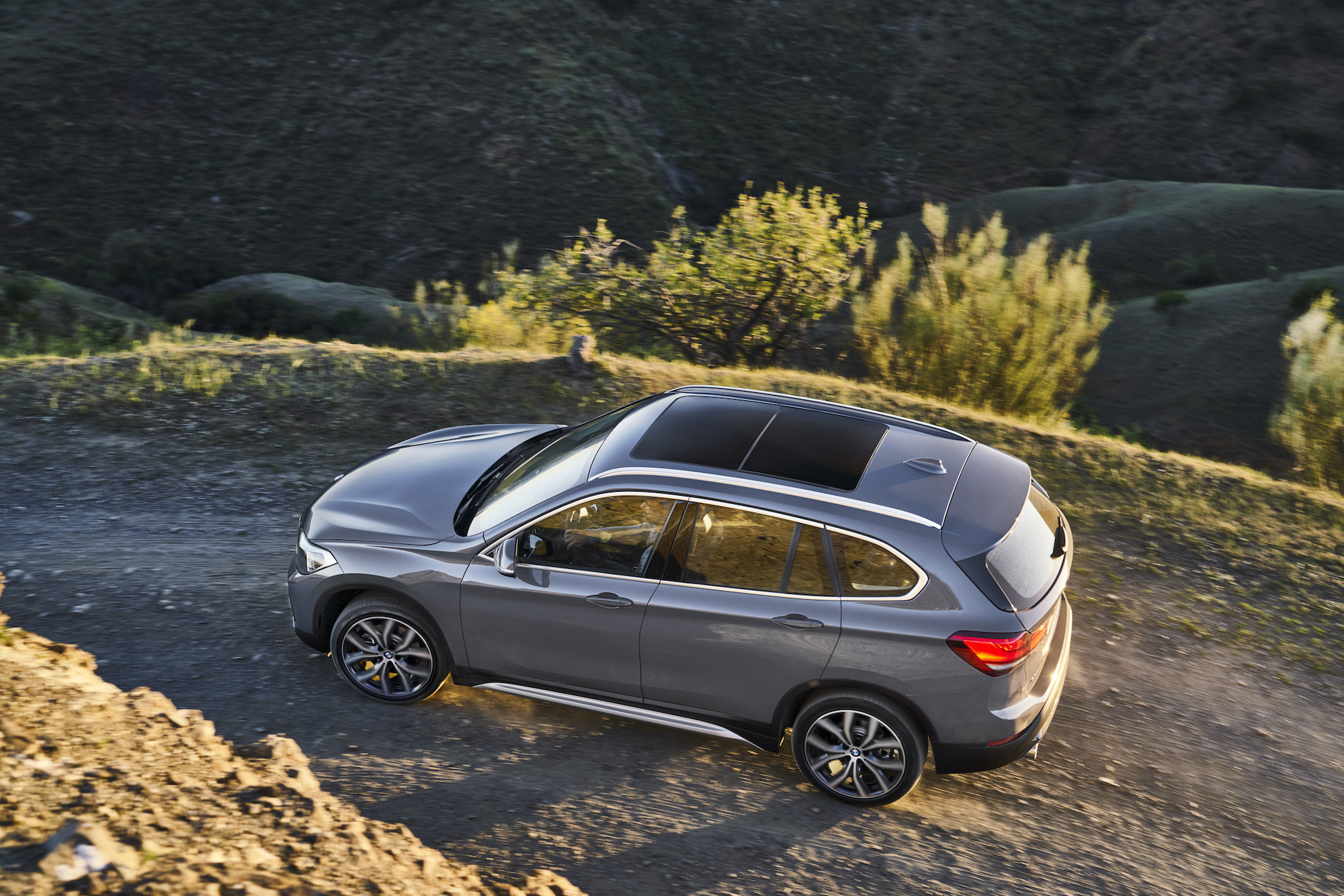 A gray BMW X1 luxury SUV travels on a dirt road on a mountain