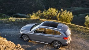 A gray BMW X1 luxury SUV travels on a dirt road on a mountain
