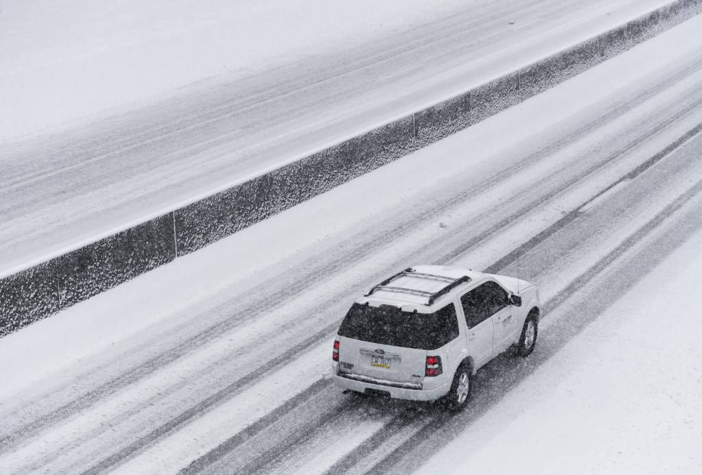 A white Ford Expedition SUV travels on a snowy highway.