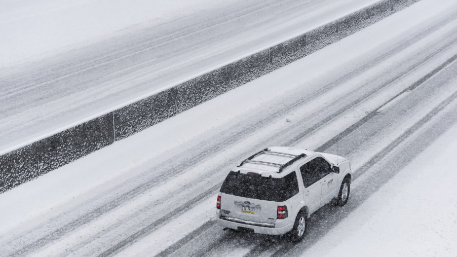 A white Ford Expedition SUV travels on a snowy highway.