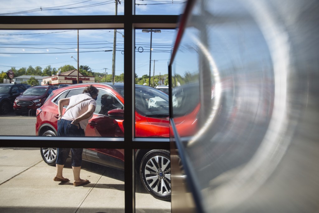 A potential customer looks in the window a new red car at a dealership.