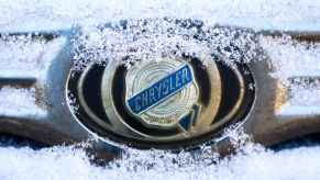 A Chrysler car emblem is covered with snow on a car