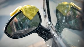 A yellow microfiber towel rests on the sideview mirror of a wet car